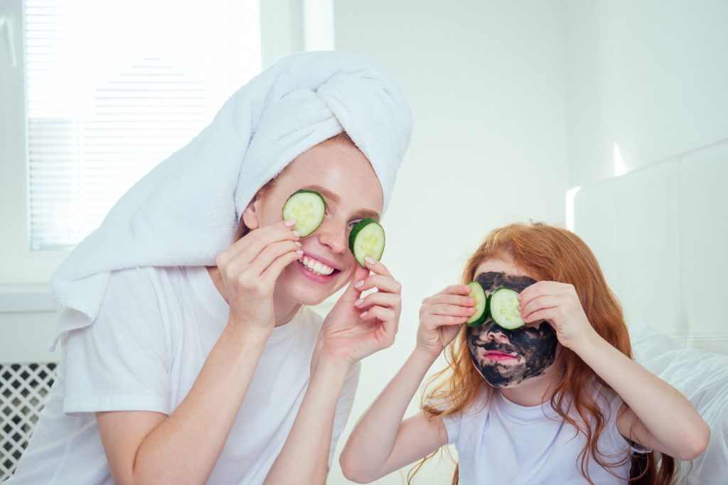 A mother and daughter with cucumbers on their eyes and the daughter with a face mask on