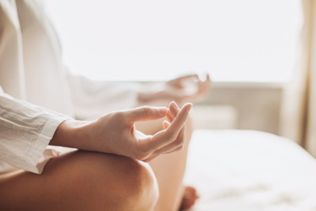A woman meditating at home with her hands resting on her knees