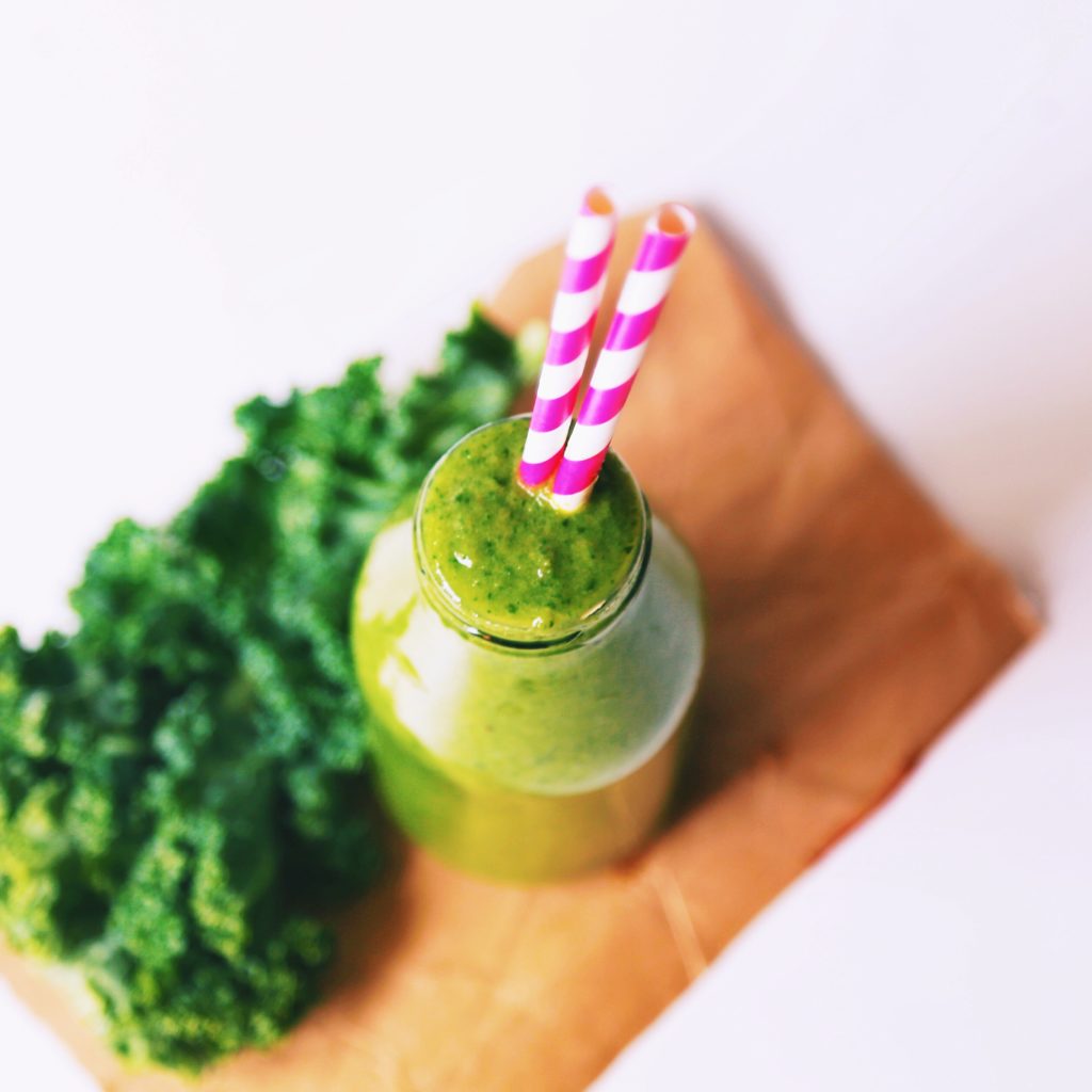 Green smoothie with kale and a pink and white straw