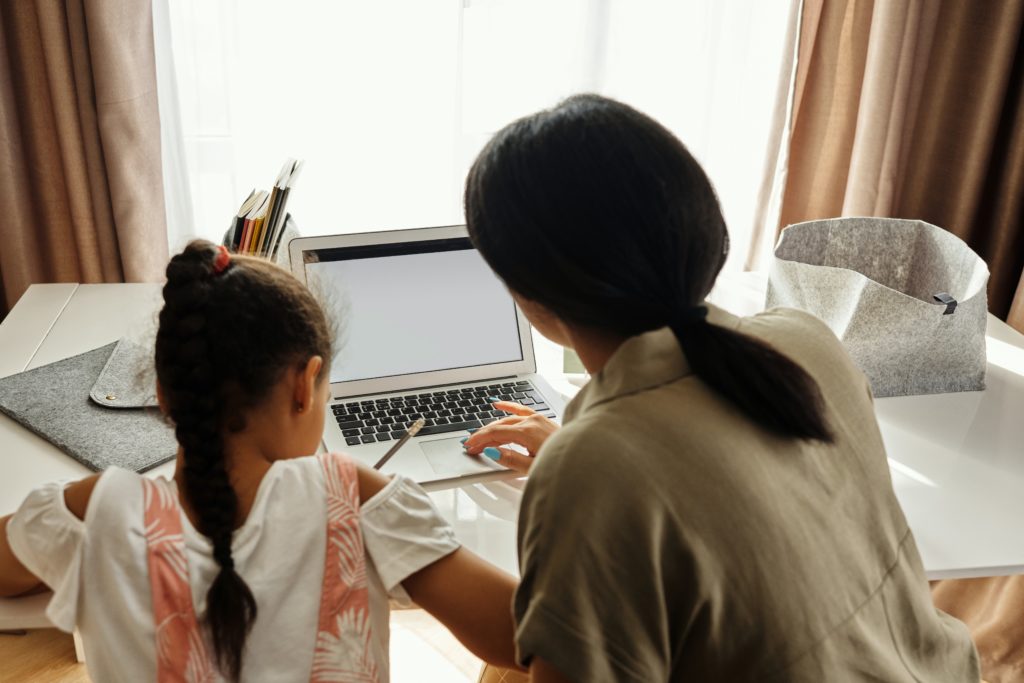 Mother and daughter at a computer, virtually leaning at a desk with school supplies. 