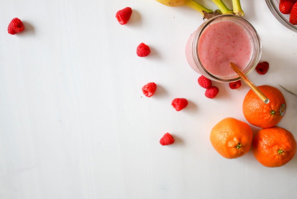 A smoothie with banana, oranges, raspberries displayed on a white background.