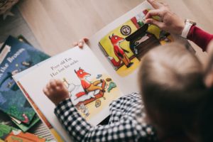 A child reading a book featuring a fox sitting on the floor