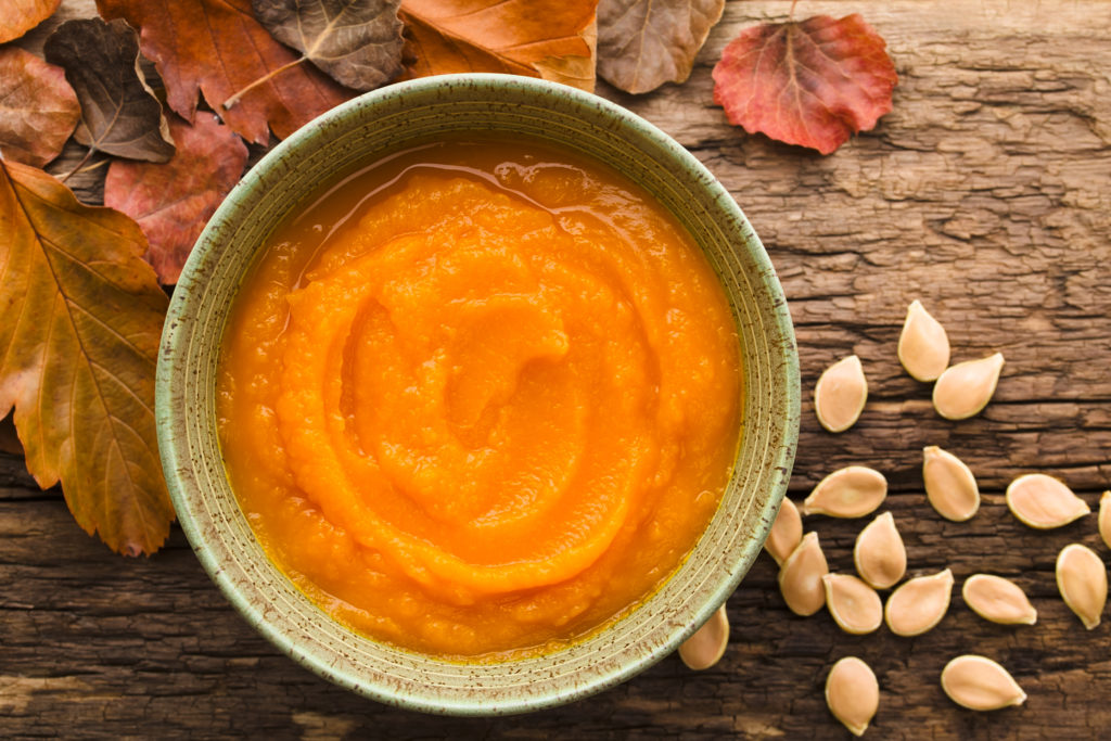 Pumpkin puree in a green bowl on a table with pumpkin seeds and fall leaves