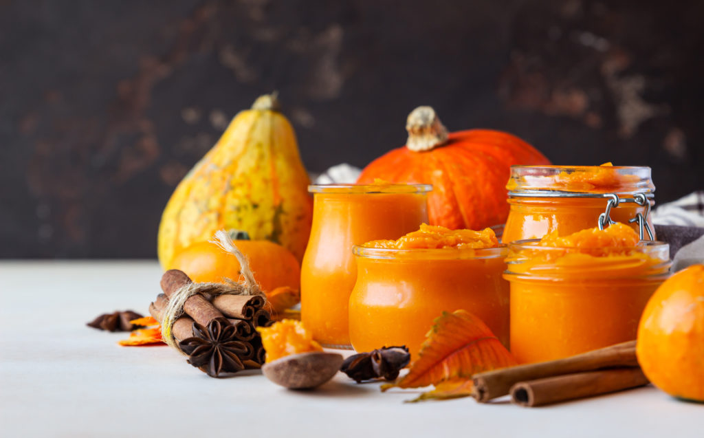 Pumpkin and gourds on a table with fall spices and pumpkin puree in mason jars