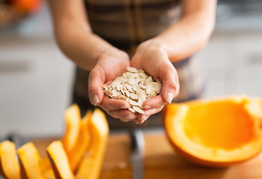 A woman scooped pumpkin seeds out of pumpkin and is holding them in both hands