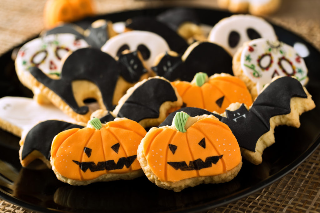 A black bowl full of Halloween cookies featuring a jack-o-lantern, bat and skeletons