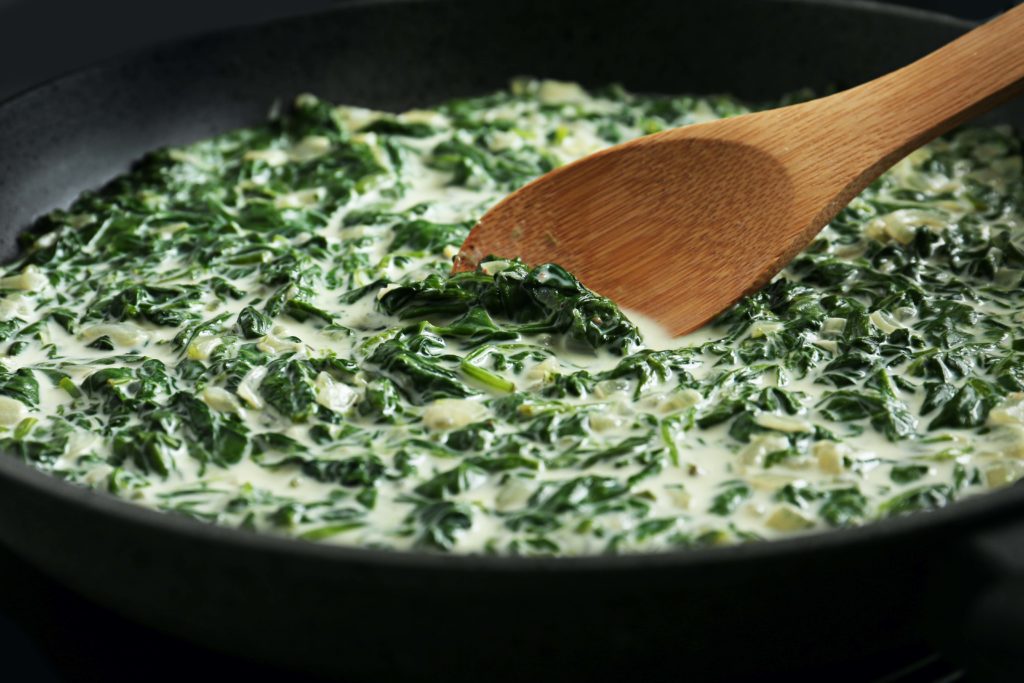 Creamed spinach with a wooden spoon in a black bowl