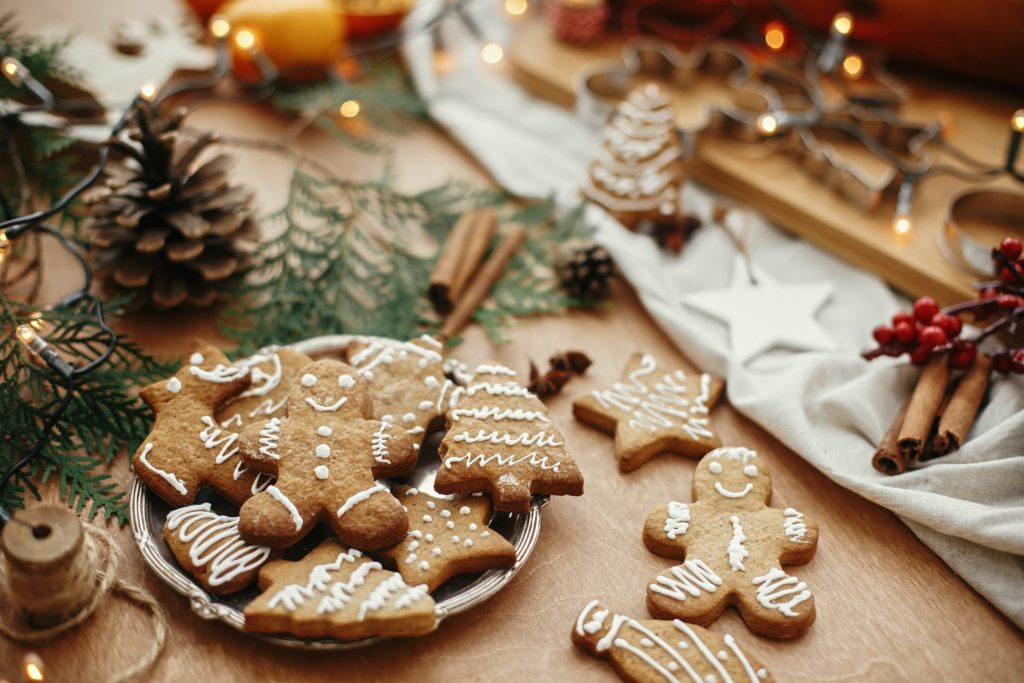 Christmas gingerbread cookies with cinnamon, pine cones, cedar branches with golden lights on rustic table