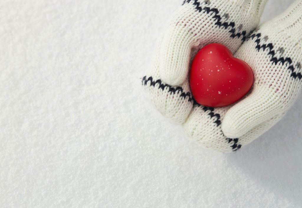 Winter snow background, close up of little girls hands holding red rubber heart