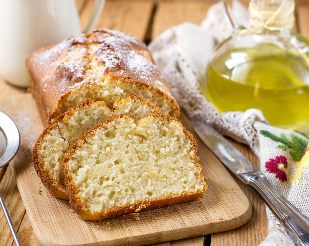 Sliced olive oil cake on a wood board with a container of olive oil