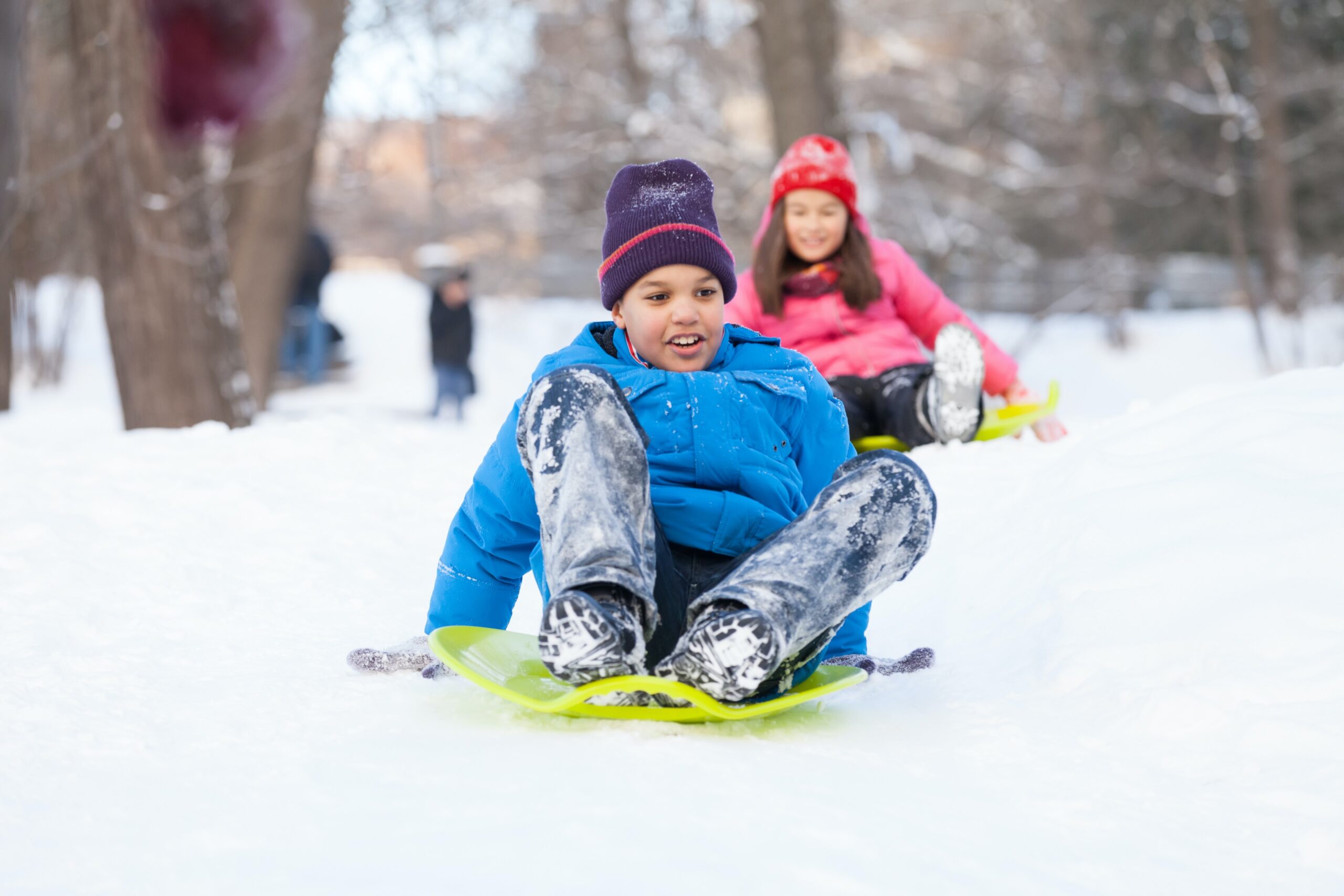 boy and girl sliding on sledges in park. two children sitting on sledges and speeding down
