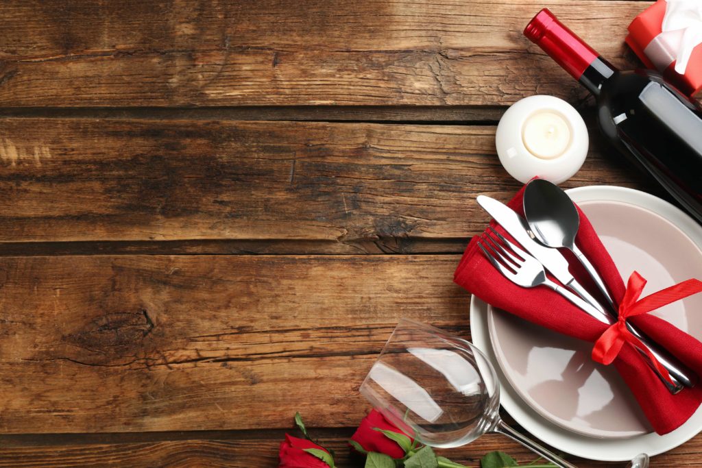 Valentine's Day dinner set up on a wooden table with red napkin and wine bottle 