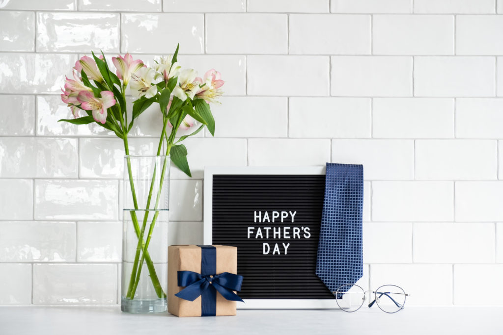 Happy Father's Day sign with flowers, gift, tie and glasses on a kitchen backsplash