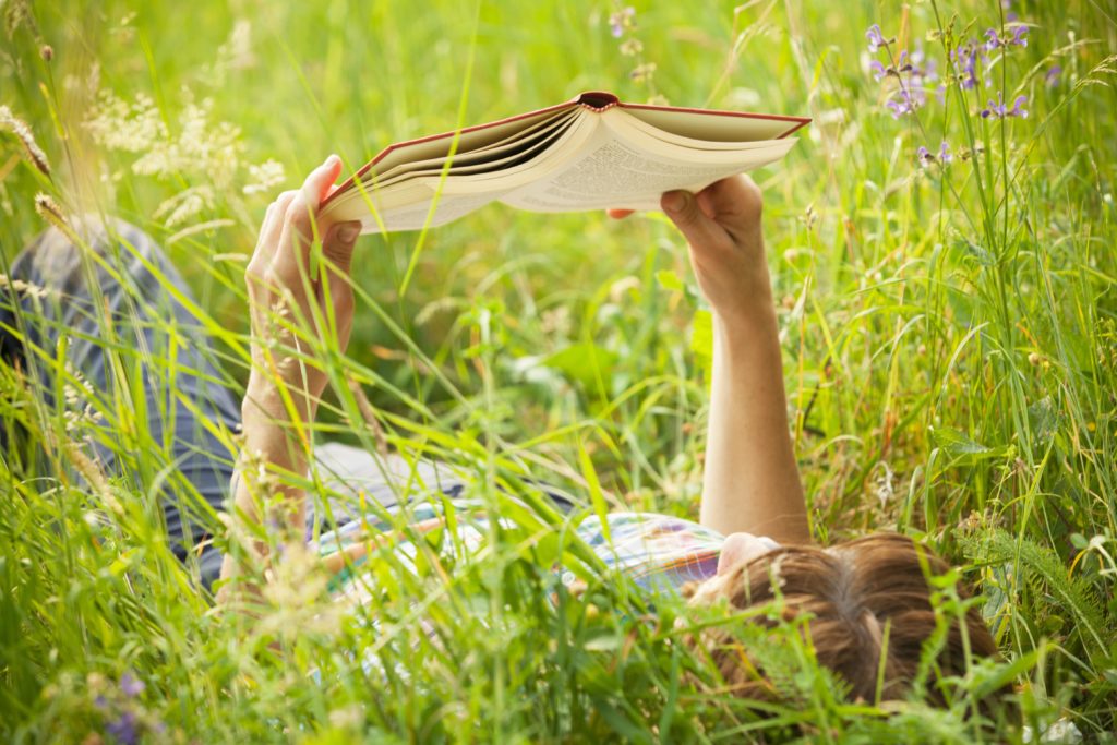 A girl reading outside laying in tall grass 