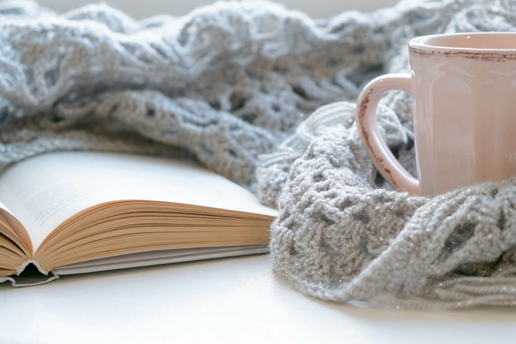 A closeup of a book, blanket and coffee mug creating a cozy home vibe