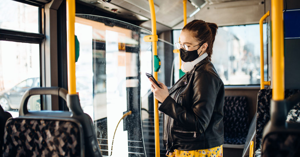 Woman standing on public transit wearing a mask holding a phone in her hand