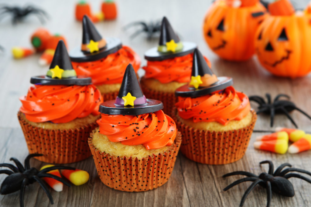 halloween cupcakes, orange frosting with witch hats on a table with candy corn, spiders, jack-o-lantern