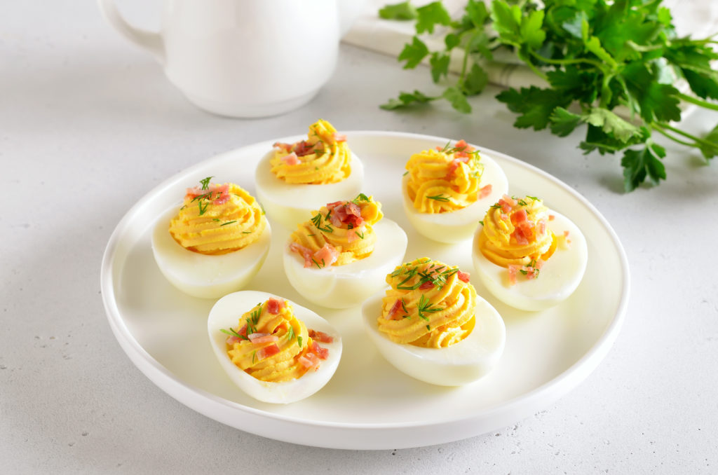 Stuffed eggs with egg yolk, bacon, mustard and dill, close up view on a white dish
