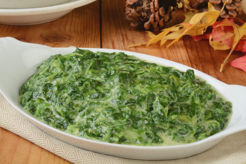 A small casserole dish of spinach in cream sauce with fall table decor like leaves and pinecones