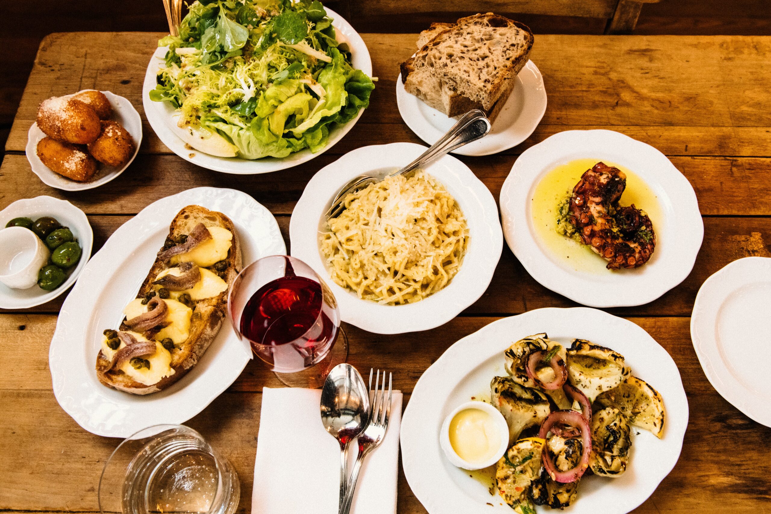 plates of different entrees on a wooden table with a glass of wine