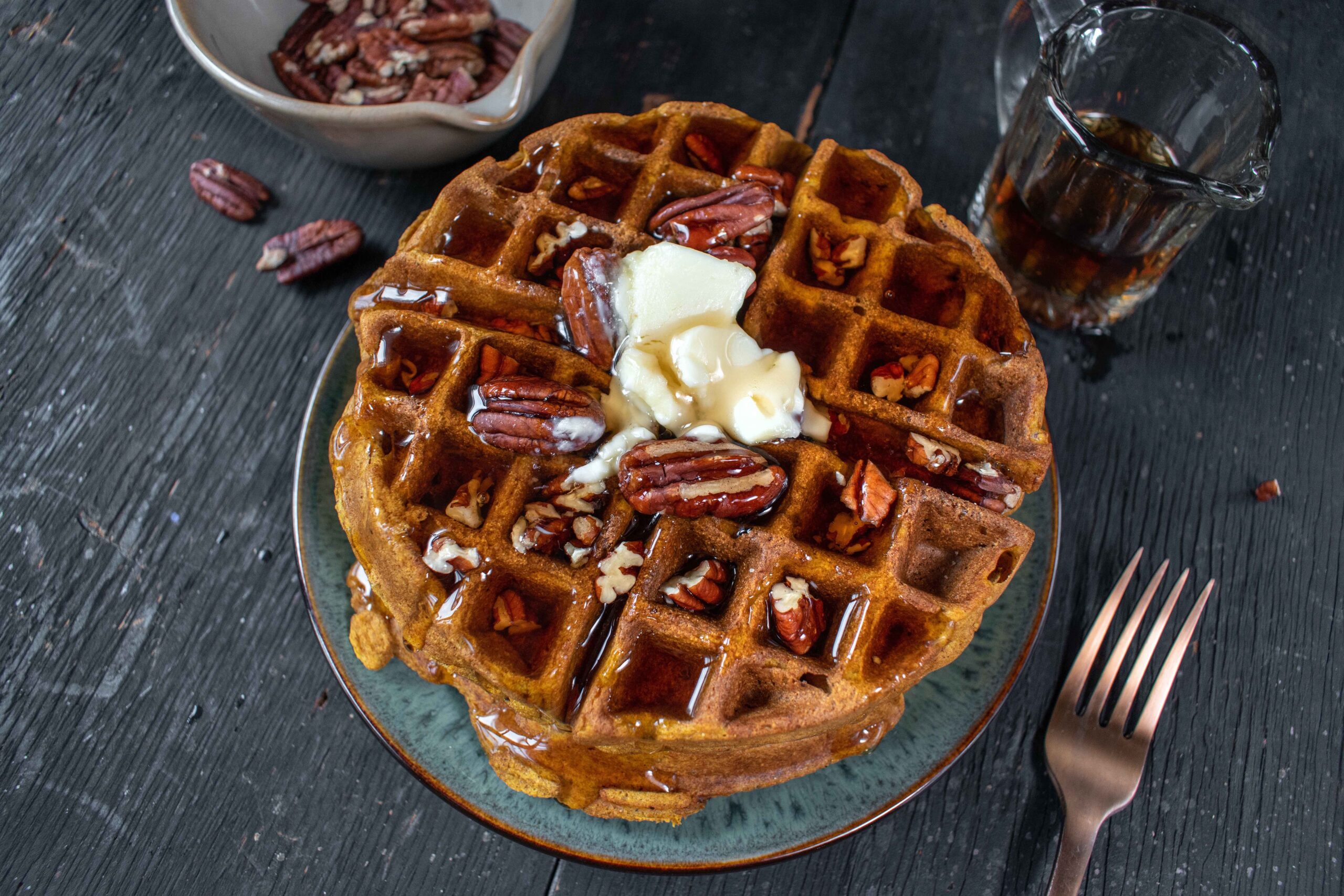 A close up on a pumpkin waffle on a table with pecans and whipped cream