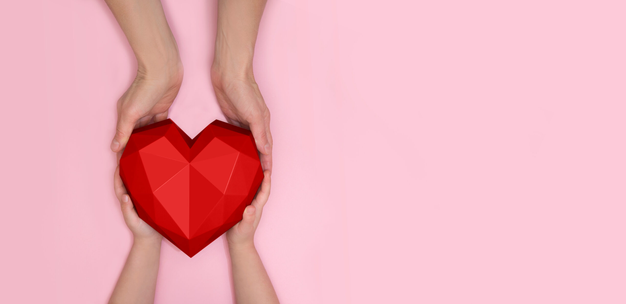 Pink background with two hands holding a red heart sculpture 