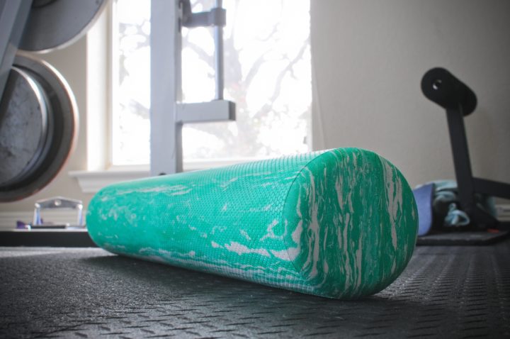 A close up photo of a teal foam roller on a gym floor