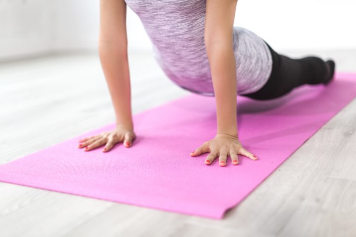 A woman doing yoga on a pink yoga mat in her home