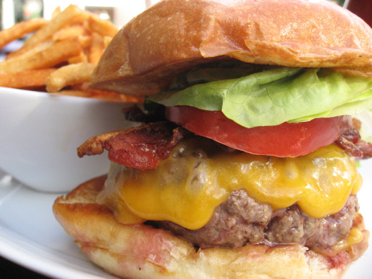 Five Napkin Burger collasol bacon cheddar burger with lettuce and tomato and a side of fries in the background