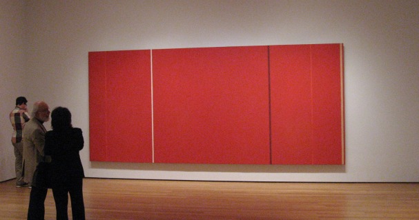 Three gallery visitors looking at the Mark Rothko piece - a large scale abstract expressionist painting mostly red with thin black and white line