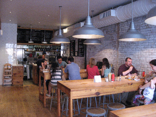 Bark Dogs NYC interior with brick walls, high wood tables with stools, industrial lights, and wood floors.