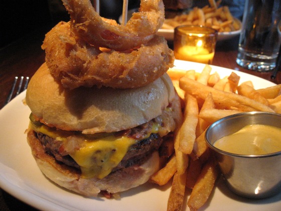 Burger & Barrel in Soho serves up a huge hamburger with cheese oozing out, two onion rings on top and a side of fries and dipping sauce