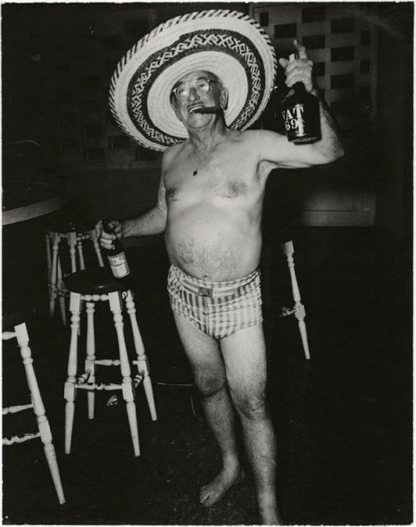 American in Cuba with a straw hat, holding alcohol in a pair of swim shorts standing in a bar before the Cuban War on display at New York's International Center for Photography