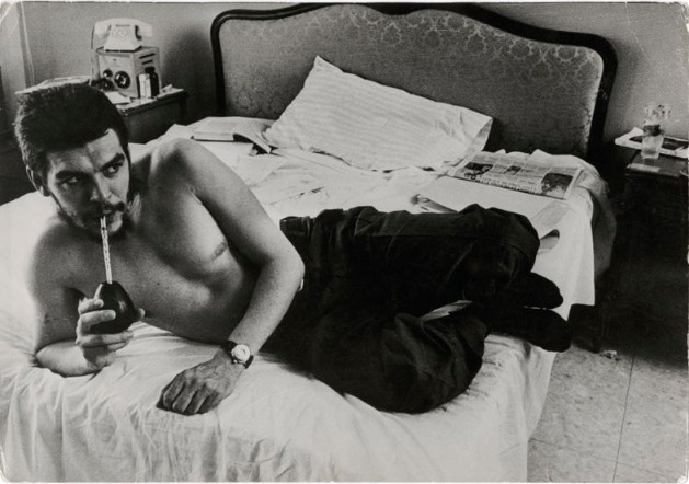 Cuban Revolutionary Che sitting on a bed sipping mate without a shirt in dark pants photograph on display at the International Center for Photography in NYC