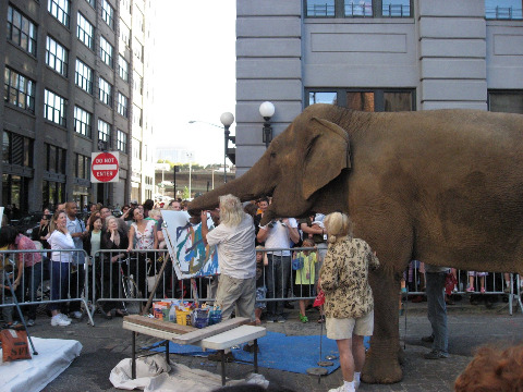 An elephant in the streets of NYC saying hello to passerbys and creating a painting wiht is trunk at the Dumbo Arts Festival
