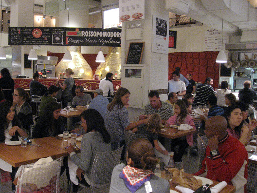 Mario Batali Restaurant NYC interior bustling with people dinning in front of the large wood burning ovens