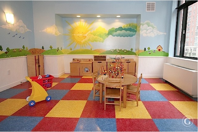 Family apartments at Glenwood with a fun landscape scene of rolling hills, trees and smiling sun, red, yellow and blue square flooring, table and chairs with toys