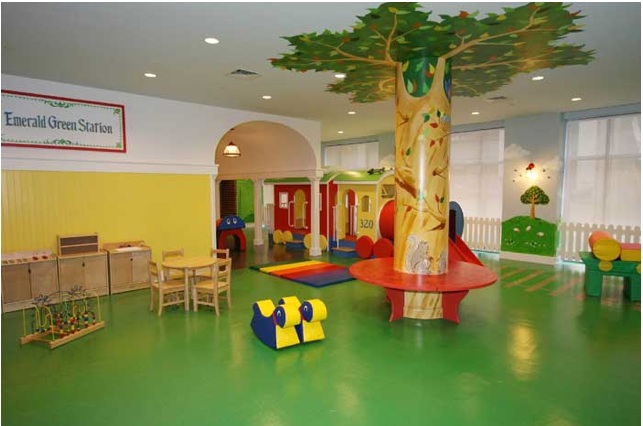 The fun Glenwood luxury family apartments features green flooring, a huge wood painted tree with circular seating, tables and chairs, bead roller coasters, and a colorful train in the background