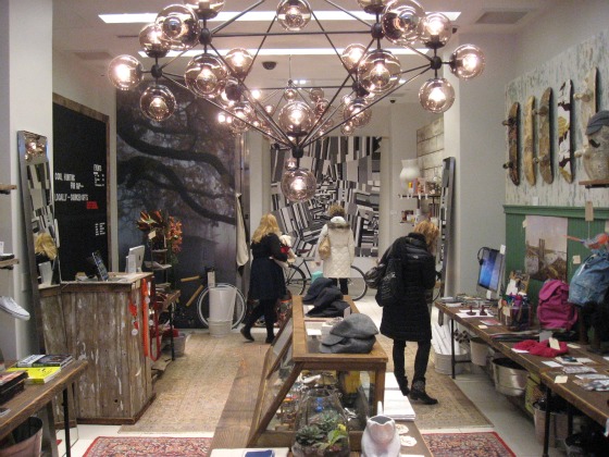 A glass an metal lamp dangles from the ceiling while three women shop at the cool hunting holiday shopping pop up