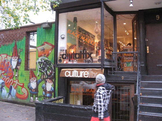 A young girl walking by the Black Market holiday shopping pop up with black trim, metal staircase leading up and a gnome graffiti wall next to it