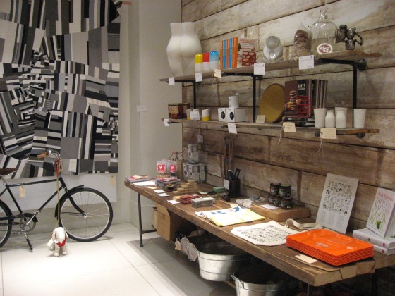 A black and white painting set behind a bike and wood shelves full of books, ceramics and other fun holiday shopping gifts