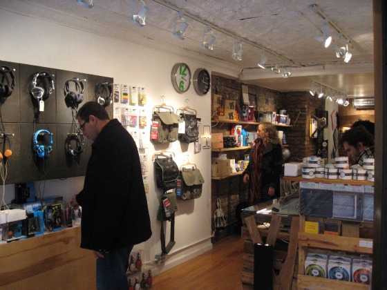 A man shopping for headphones and a woman looking at gifts on a wooden shelf at the Black Market holiday shopping pop up