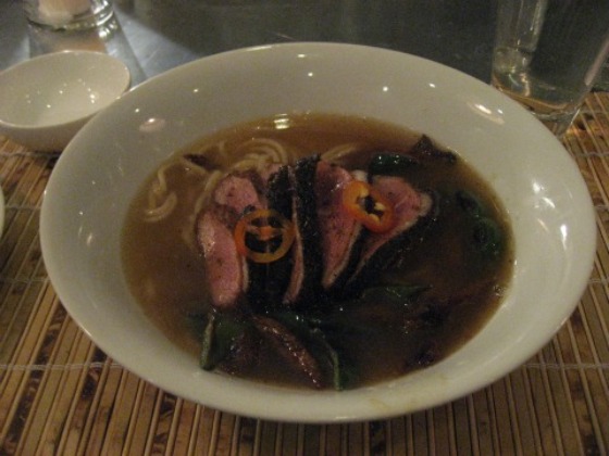 Hung Ry duck noodle soup filled with breast and leg pieces, roasted peppers in a white bowl on a bamboo placemat