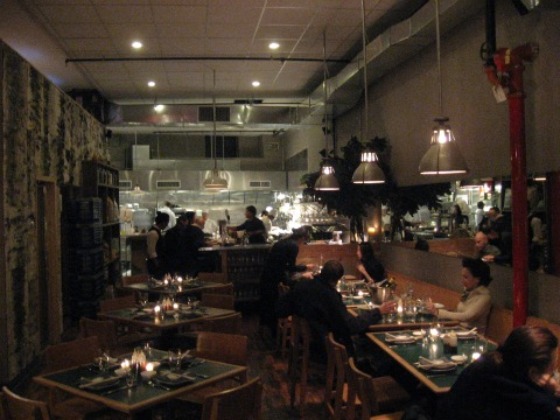 Interior of Hung Ry in NYC with drop lights over green tables, kitchen in the rear
