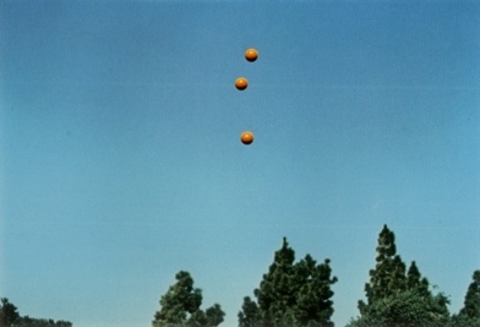 Image of 3 balls in the air set in front of a blue sky and trees art by John Baldessari