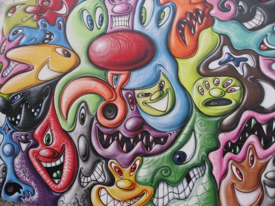 Close-up of Kenny Scharf mural with colorful cartoon faces with multiple eyes and noses and silly smiles