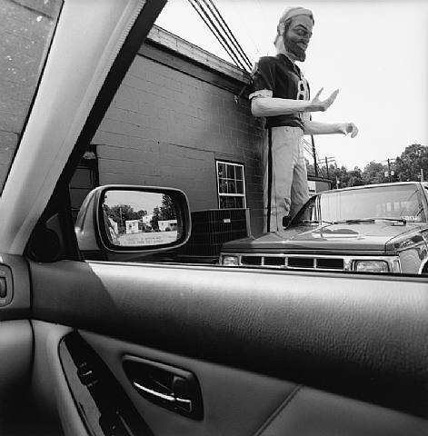 Giant sculpture of a athlete against a building framed by the passenger side window Lee Friendlander photograph