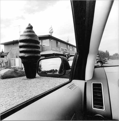 A giant ice cream cone statue is frame by the car window and mirror in this Lee Friedlander photograph