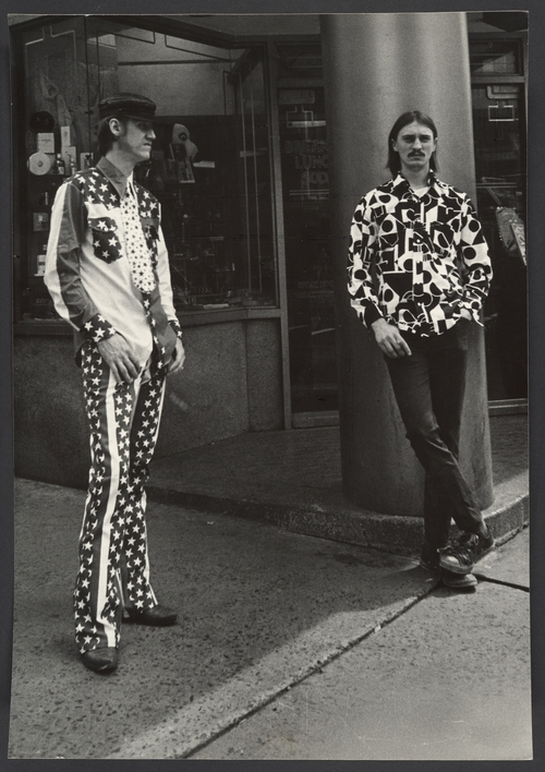 Leon Levinstein photos of NYC two men leaning against a building one in American flag print shirt and pants the other in a geometric print top with black pants