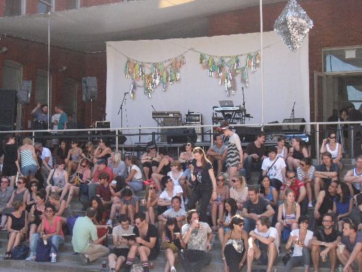 A large group on onlookers sit to watch DJ's take the stage at PS1 Warm Up party